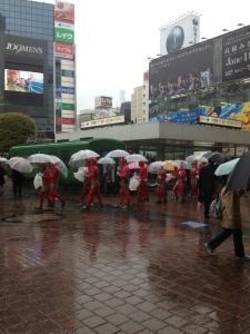 People dressed as red oni (demons) picking up trash on a wet Shibuya day!
